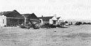 aircraft wreckage on the Wheeler flight line, in front of a fire-blackened Hangar 3 and a virtually undamaged Hangar 4