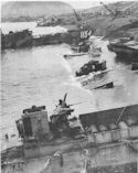 UNDER THE MENACING WALLS OF MOUNT SURIBACHI 
LANDING CRAFT UNLOAD SUPPLIES ON THE BEACHES OF EMBATTLED IWO JIMA