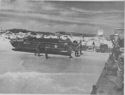 MEN AND THEIR AMPHIBIOUS TRUCKS RUSH THE UNLOADING OF A COAST GUARD MANNED TRANSPORT ON A WAVE SWEPT SICILIAN SHORE