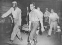 SAFELY OUT OF THE COMBAT ZONE, A COAST GUARD MANNED LST UNLOADS ITS WOUNDED ON STRETCHERS TO AMBULANCES WHICH WILL RUSH THEM TO A BASE HOSPITAL. COAST GUARDSMAN MERLE B. JEWELL (FOREGROUND), ELECTRICIAN'S MATE SECOND CLASS, OF SEATTLE, WASHINGTON, HELPS WITH A STRETCHER