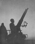 COAST GUARDSMEN ON GUN HATCH OFF THE SHORES OF SICILY. THEIR TRANSPORT CARRIES U.S. ARMY CONTINGENTS