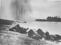 U.S. COAST GUARDSMEN AND NAVY BEACH BATTALION MEN ARE SHOWN HUGGING THE SHAKING BEACH AT PAESTERNUM, JUST SOUTH OF SALERNO, AS A NAZI BOMBER UNLOADS ON THEM