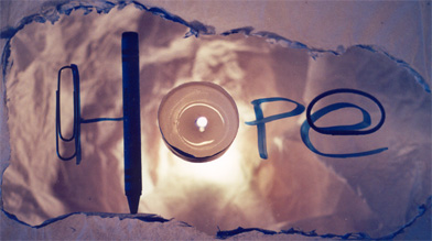The word HOPE glowing and made out of a candle, paper clip, crayon, and rubber band.  Call 211 for social services.