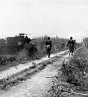 INFANTRYMEN ADVANCING ALONG A ROAD ON SAIPAN