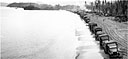 Trucks lined up along the water's edge have just been unloaded from the LST in the background