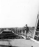 U.S. INFANTRYMEN CROSSING A DAMAGED BRIDGE as they advance inland from the beach