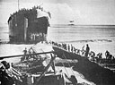 THE BEACH AT CAPE SANSAPOR, DUTCH NEW GUINEA, WAS NOT MADE TO ORDER FOR THE AMERICAN INVADERS, SO TROOPS 'TURNED TO' TO BUILD A RAMP OUT TO THE YAWNING BOW DOORS OF THE COAST GUARD MANNED LST-18